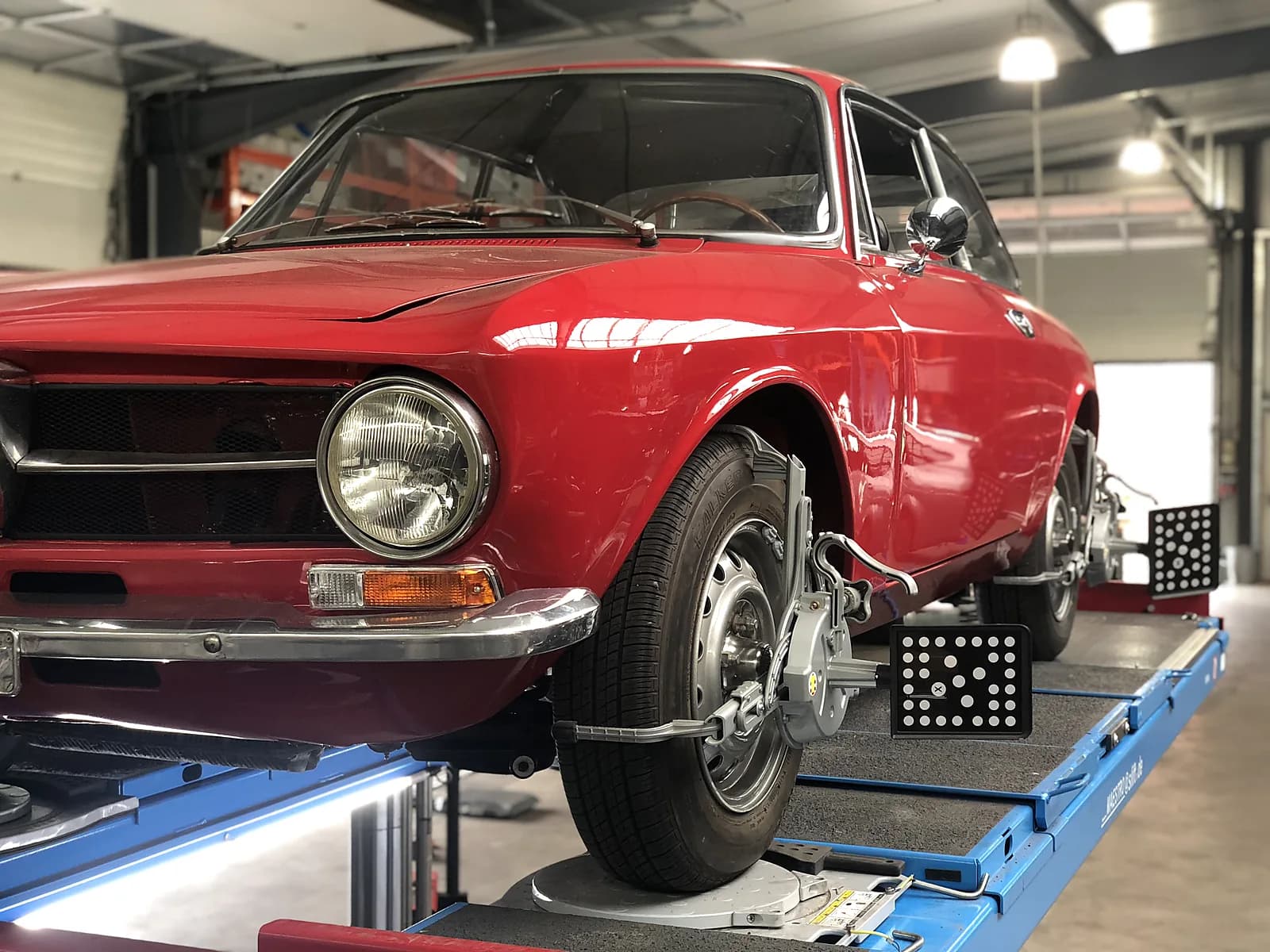 Roter Alfa Romeo Oldtimer auf Hebebühne mit montierten Achsvermessungs-Targets an den Rädern