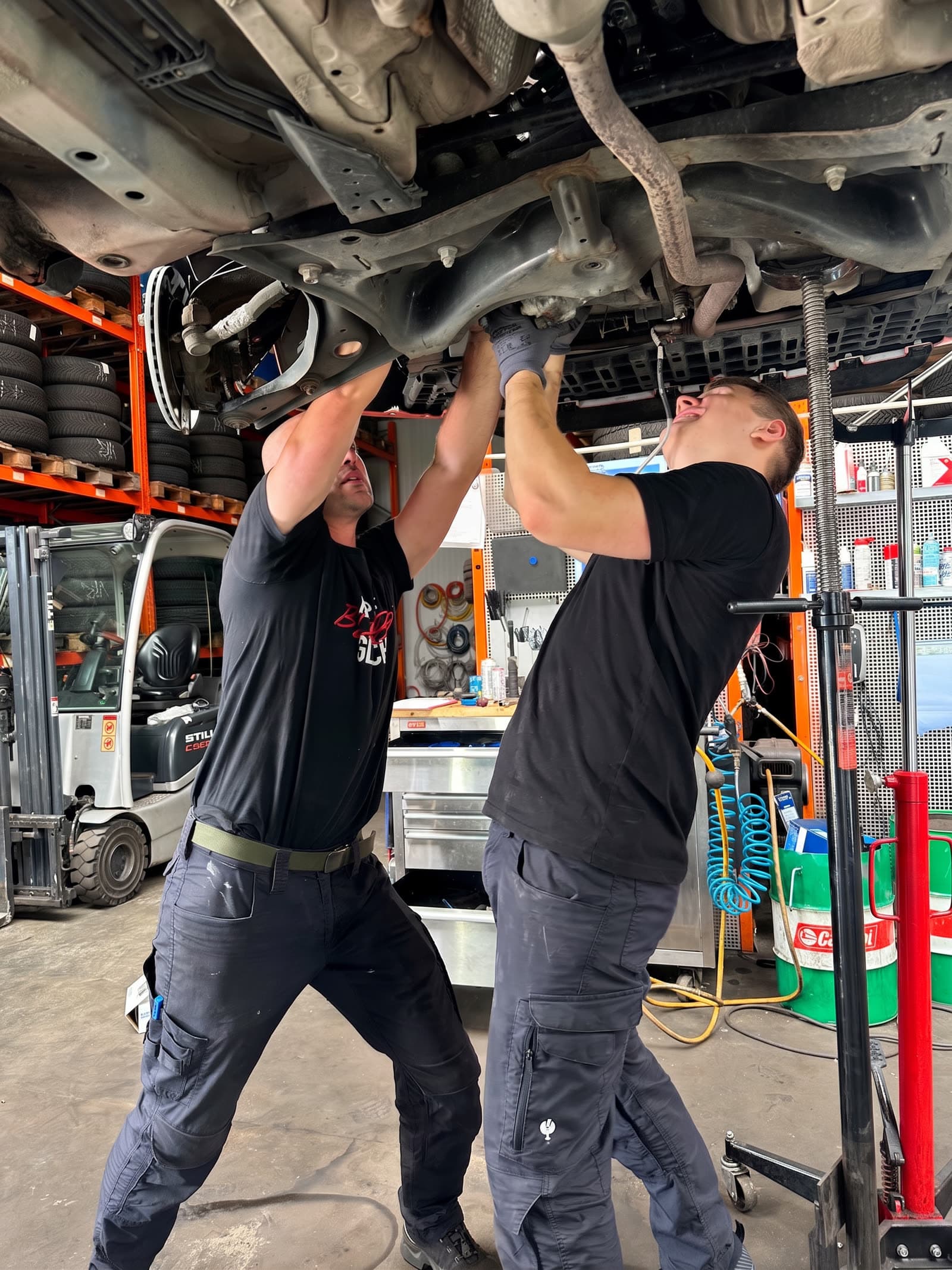 Zwei StarWash-Mechaniker arbeiten gemeinsam am Auspuff unter einem Fahrzeug auf der Hebebühne